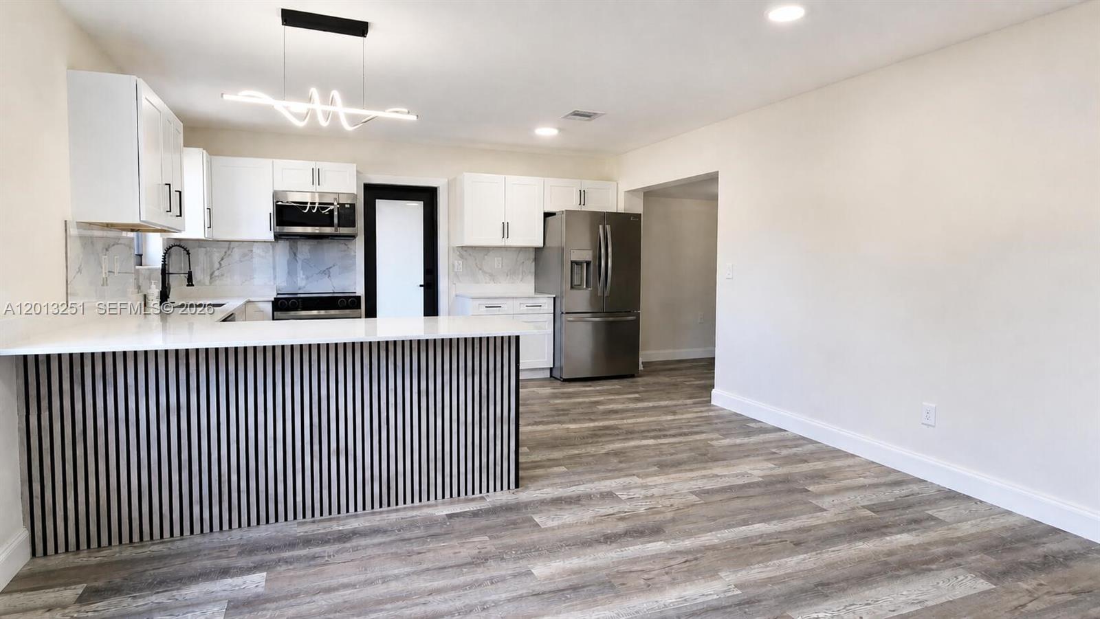 A modern kitchen features white cabinets, stainless steel appliances, and a slatted wood kitchen island — 7181 Raleigh St, Hollywood FL 33024, HOLLYWOOD, FL