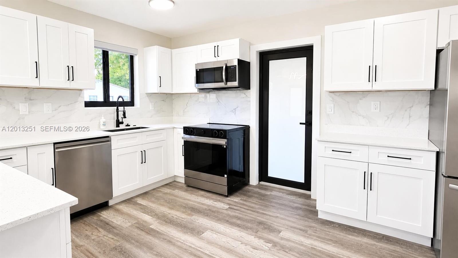 A modern kitchen features white cabinets, stainless steel appliances, and a black-framed glass door — 7181 Raleigh St, Hollywood FL 33024, HOLLYWOOD, FL
