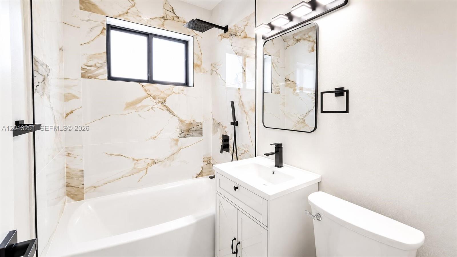 A bathroom features a white vanity, a bathtub, and walls with marble-patterned tile — 7181 Raleigh St, Hollywood FL 33024, HOLLYWOOD, FL