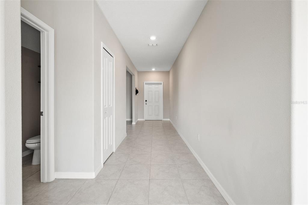 A hallway with light tile flooring, white walls, and doors leading to a bathroom and entrance — 5553 TURKEY CREEK WAY, LAKELAND, FL
