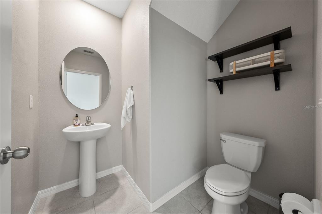 A small bathroom features a pedestal sink, a round mirror, and a toilet with shelving — 5553 TURKEY CREEK WAY, LAKELAND, FL