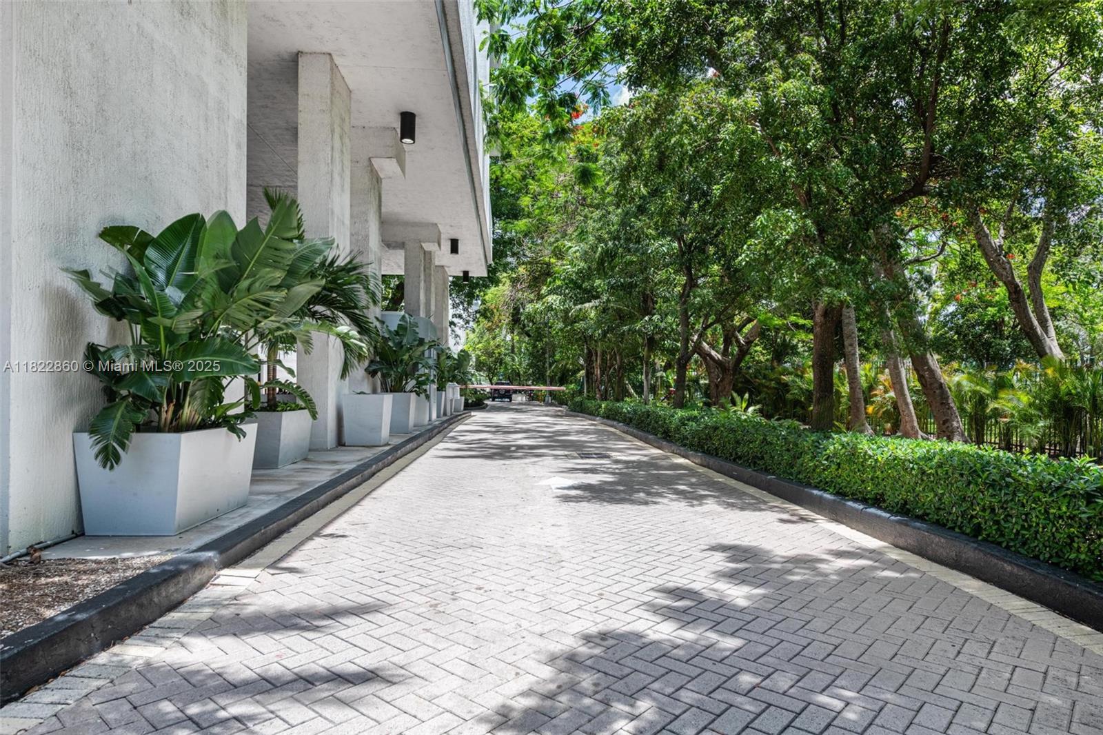 A paved driveway leads toward a building entrance lined with large potted plants and trees — 1861 NW S River Dr # 01, Miami FL 33125, MIAMI, FL