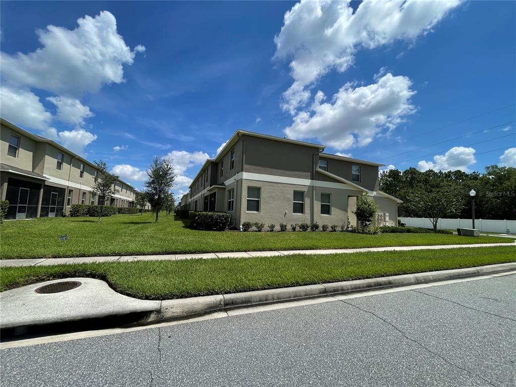 A multi-story tan townhouse building sits on a grassy lawn next to a paved road — 15246 HARRINGTON COVE DRIVE, ORLANDO, FL