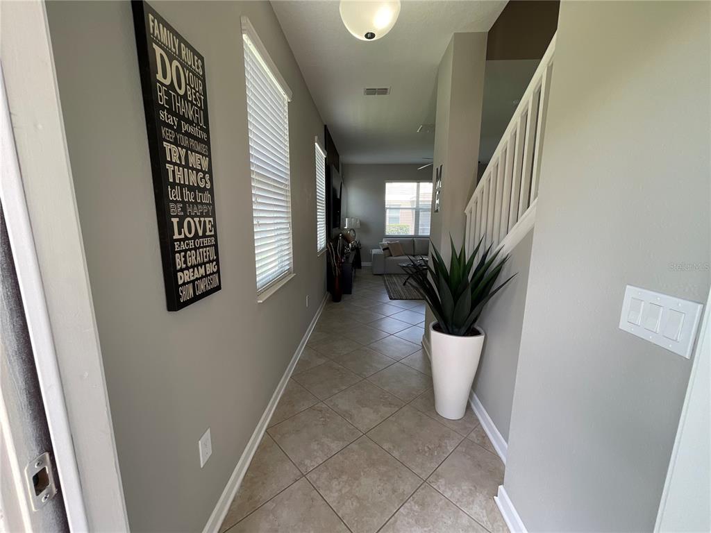A tiled hallway leads to a living area with a staircase and wall decor — 15246 HARRINGTON COVE DRIVE, ORLANDO, FL