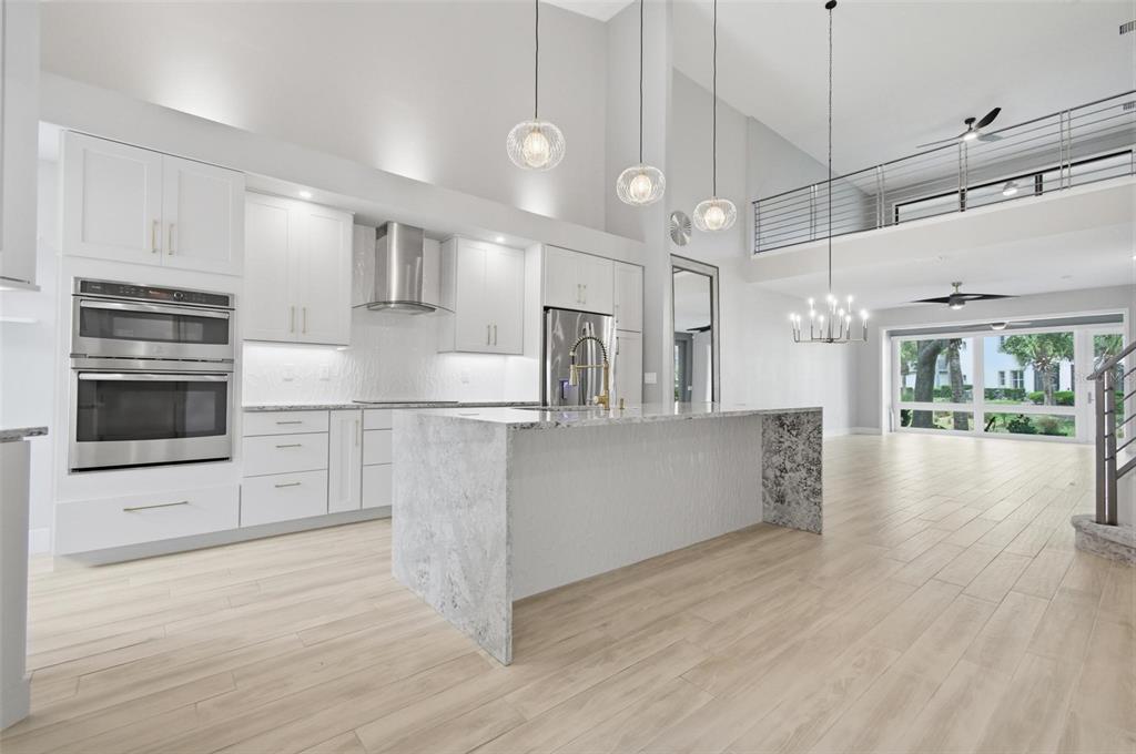 A modern kitchen features white cabinetry, a granite waterfall island, and a lofted upper level — 19 RIVER LANDING DRIVE, PALM COAST, FL