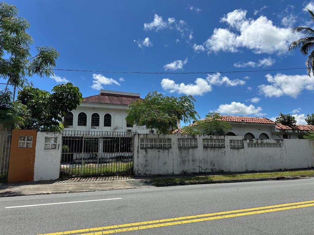 A two-story white building with arched windows sits behind a tall concrete wall and fence — 5 Calle 519 QB6 URBANIZACIÓN COUNTRY CLUB, CAROLINA, PR