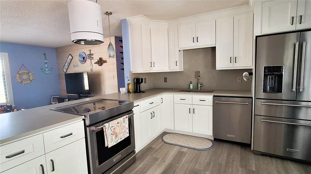A kitchen with white cabinets, stainless steel appliances, and light wood-look flooring — 40 SE CHINICA DRIVE, SUMMERFIELD, FL