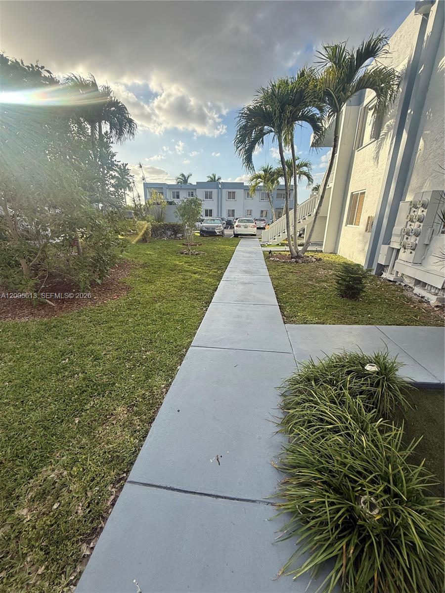 A concrete walkway leads through a grassy courtyard toward a multi-story apartment building — 6219 SW 131st Pl # 204, Miami FL 33183, MIAMI, FL