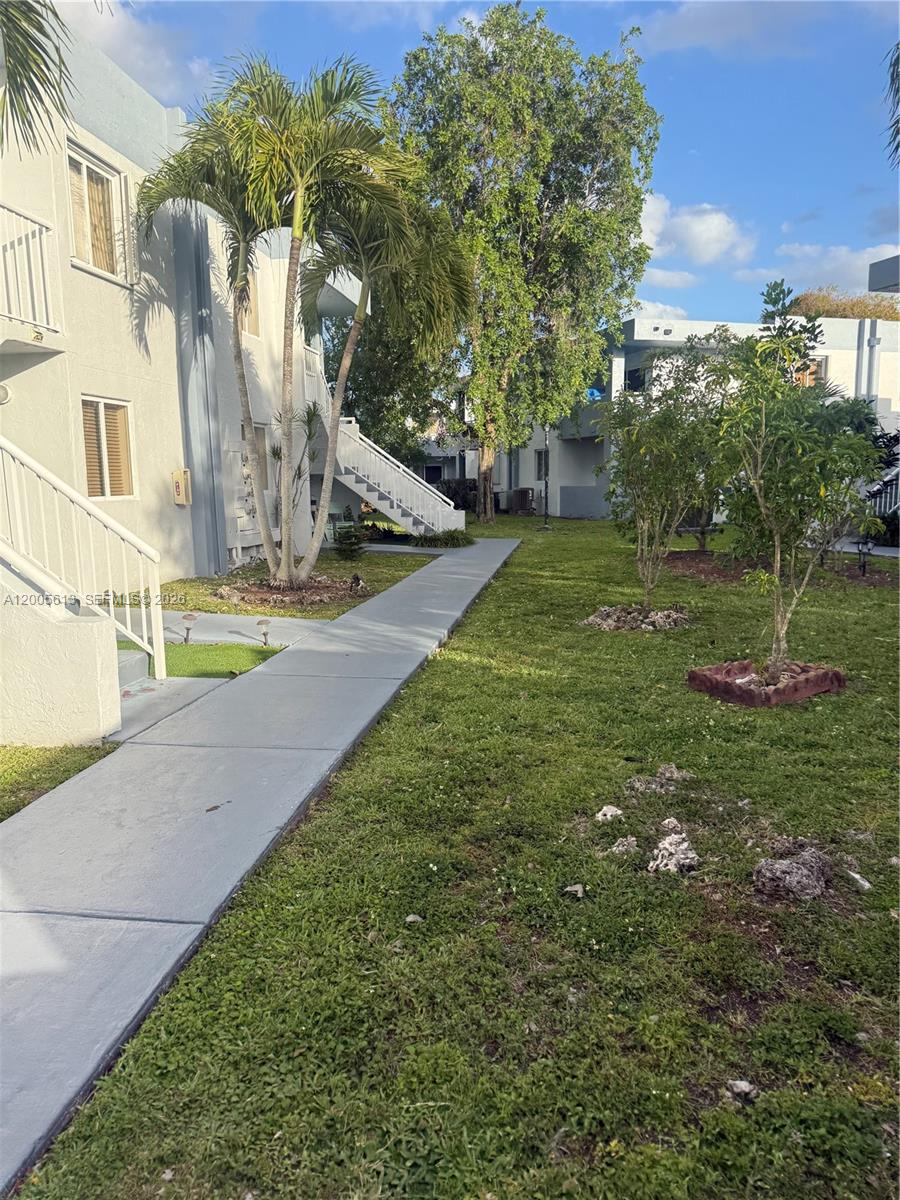 A concrete walkway leads past a multi-story apartment building and a grassy lawn with trees — 6219 SW 131st Pl # 204, Miami FL 33183, MIAMI, FL