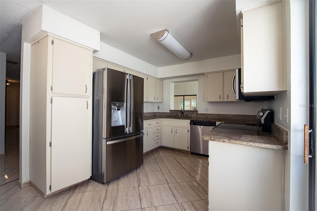 A kitchen features stainless steel appliances, light-colored cabinets, granite countertops, and diagonal tile flooring — 3429 PINEBROOK COURT, ORLANDO, FL