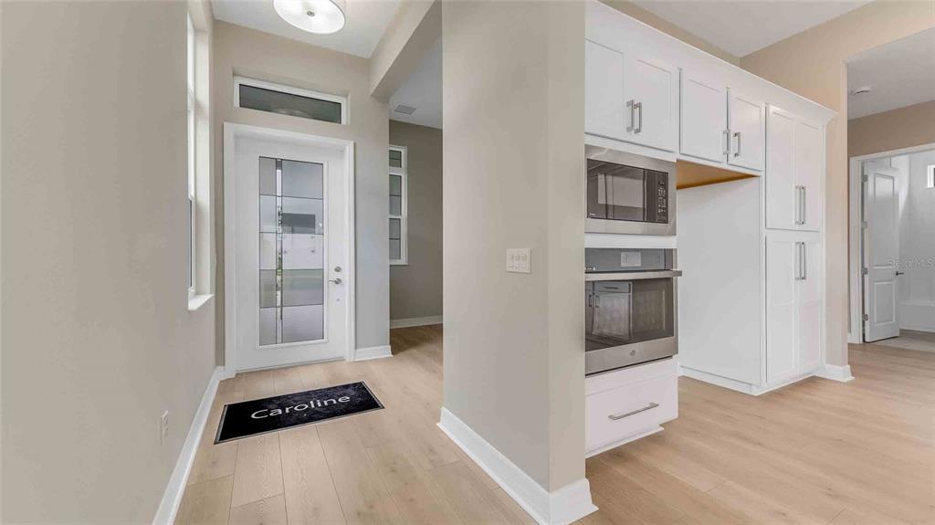 An entryway with light wood floors leads to a kitchen featuring white cabinets and appliances — 889 MEGANO BOULEVARD, DELAND, FL