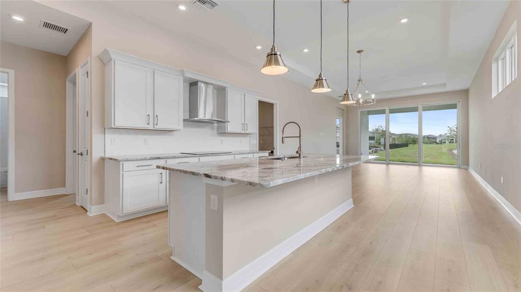 A modern kitchen features white cabinets, a marble-topped island, and light wood flooring — 889 MEGANO BOULEVARD, DELAND, FL