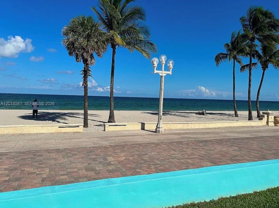 A paved walkway overlooks a sandy beach with palm trees and a lamp post — 3400 N Surf Rd # 1, Hollywood FL 33019, HOLLYWOOD, FL