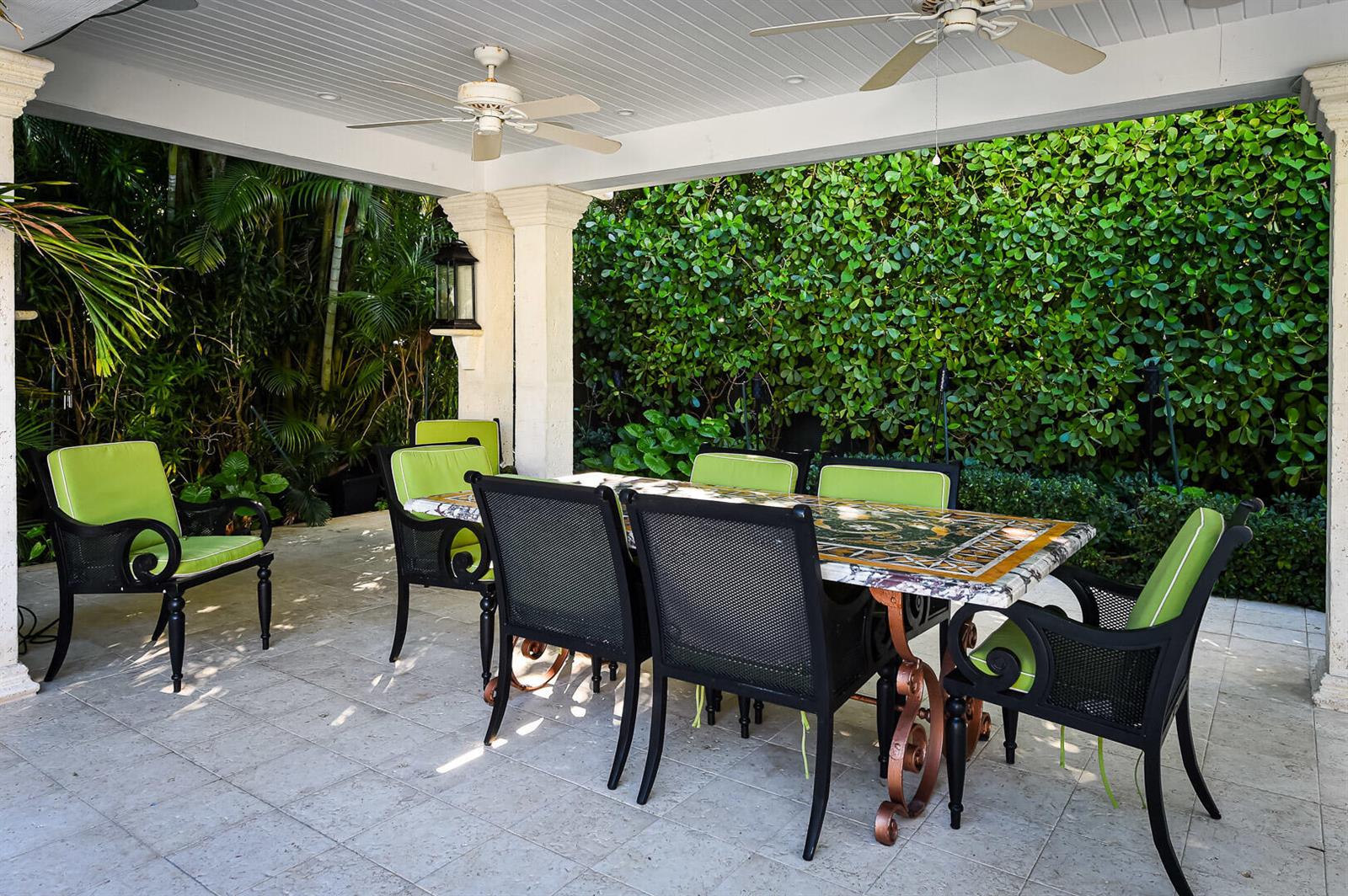 A covered outdoor patio features a stone-topped dining table with black chairs and green cushions — 202 Coral Lane, Palm Beach FL 33480, PALM BEACH, FL