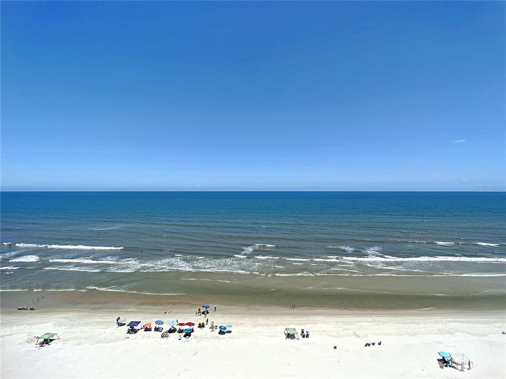 An elevated view of a sandy beach with colorful umbrellas and the ocean beyond — 5207 S ATLANTIC AVENUE UNIT 822, NEW SMYRNA BEACH, FL