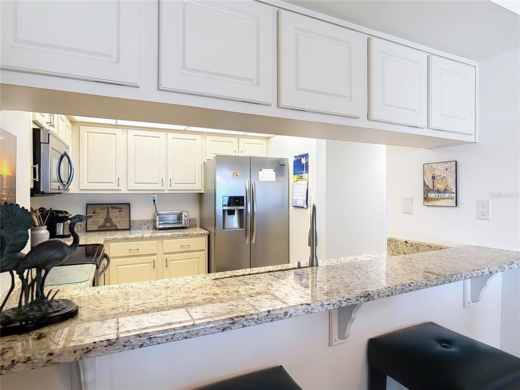 A kitchen features white cabinets, granite countertops, and a breakfast bar with black stools — 5207 S ATLANTIC AVENUE UNIT 822, NEW SMYRNA BEACH, FL