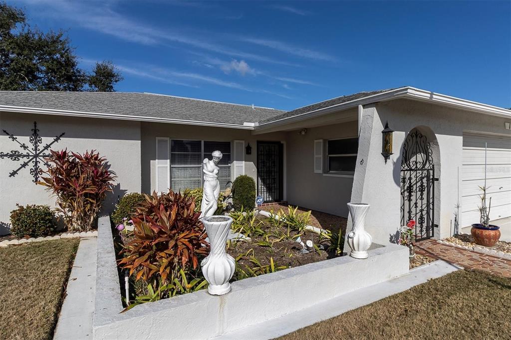 The front exterior of a single-story house features a raised garden bed with statues — 10721 FOOTPRINT LANE, PORT RICHEY, FL