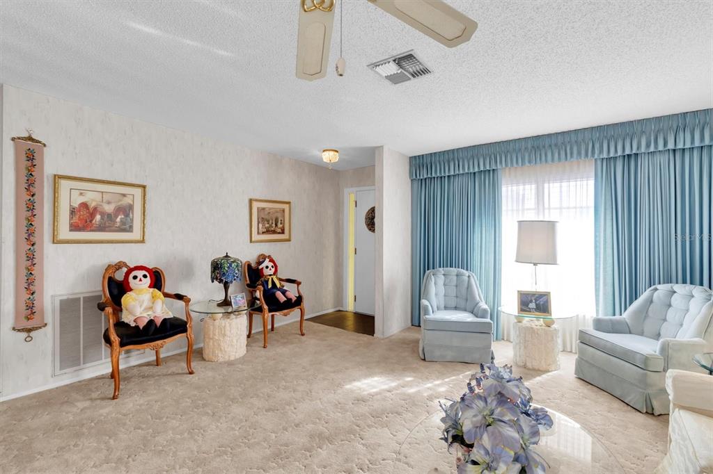 A living room features beige carpeting, blue floor-to-ceiling curtains, and two pairs of matching chairs — 10721 FOOTPRINT LANE, PORT RICHEY, FL