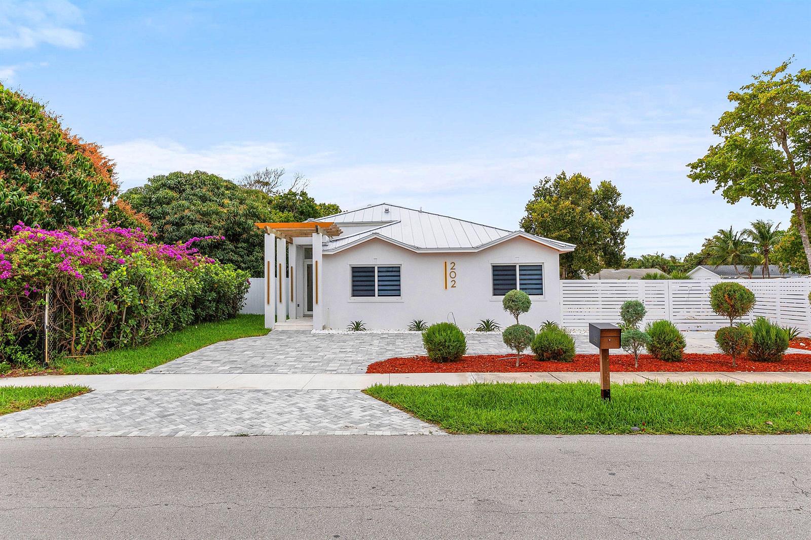 A white single-story house with a metal roof, paved driveway, and landscaped front yard — 202 SE 4th Street, Delray Beach FL 33483, DELRAY BEACH, FL