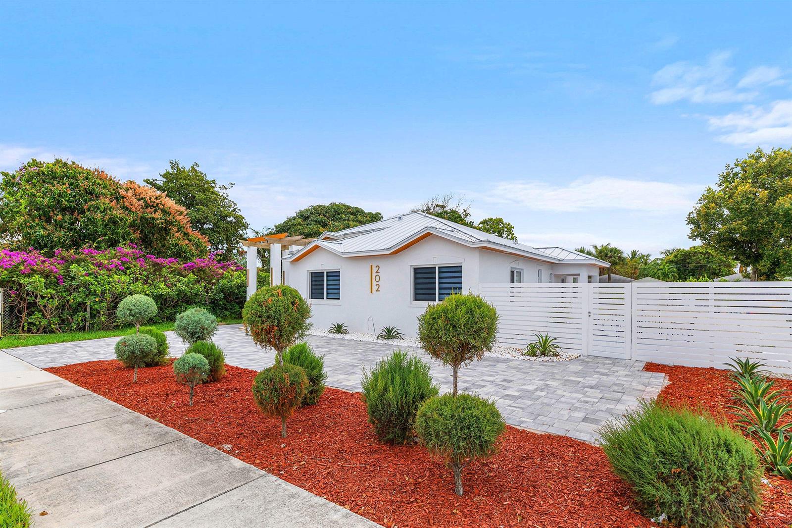 A white house with a metal roof and a paved driveway sits behind landscaped mulch — 202 SE 4th Street, Delray Beach FL 33483, DELRAY BEACH, FL