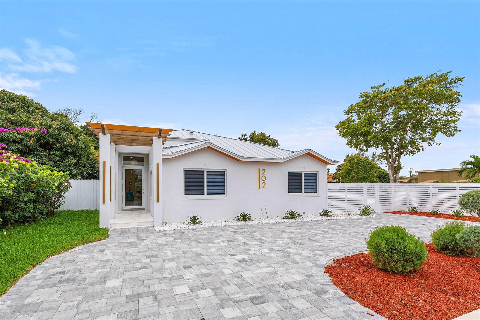 A single-story white house with a metal roof, pergola entryway, and paved driveway — 202 SE 4th Street, Delray Beach FL 33483, DELRAY BEACH, FL