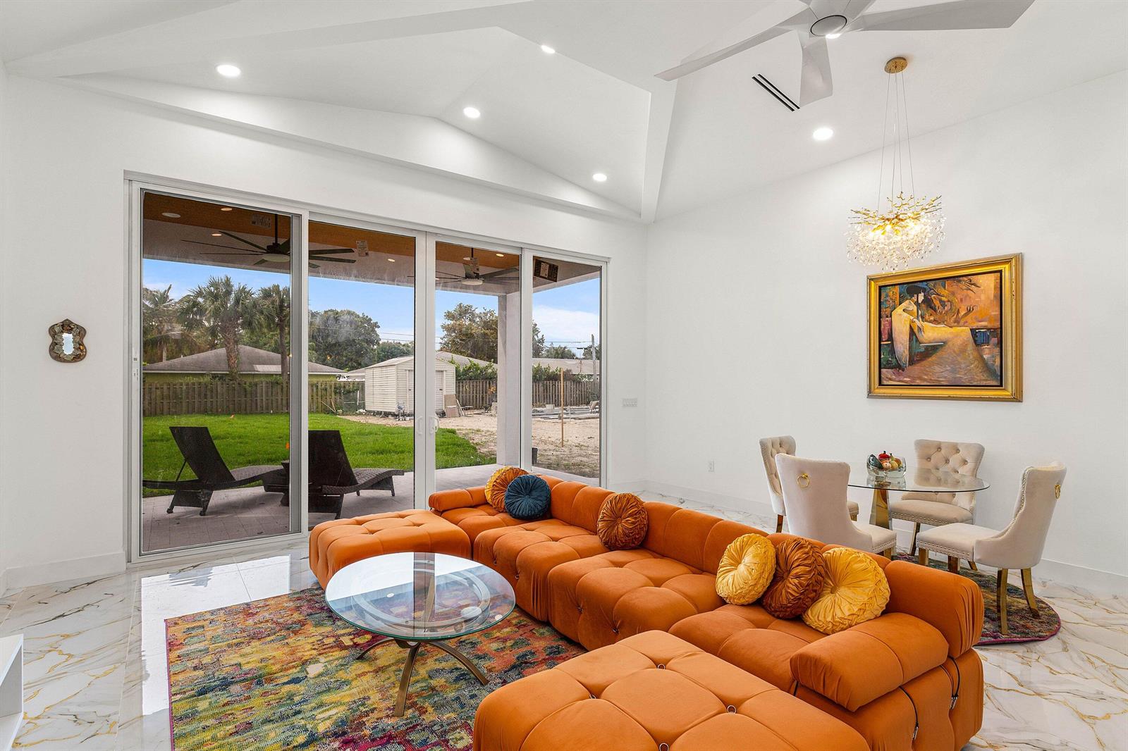 A bright living room features a large orange sectional, marble floors, and sliding glass doors — 202 SE 4th Street, Delray Beach FL 33483, DELRAY BEACH, FL