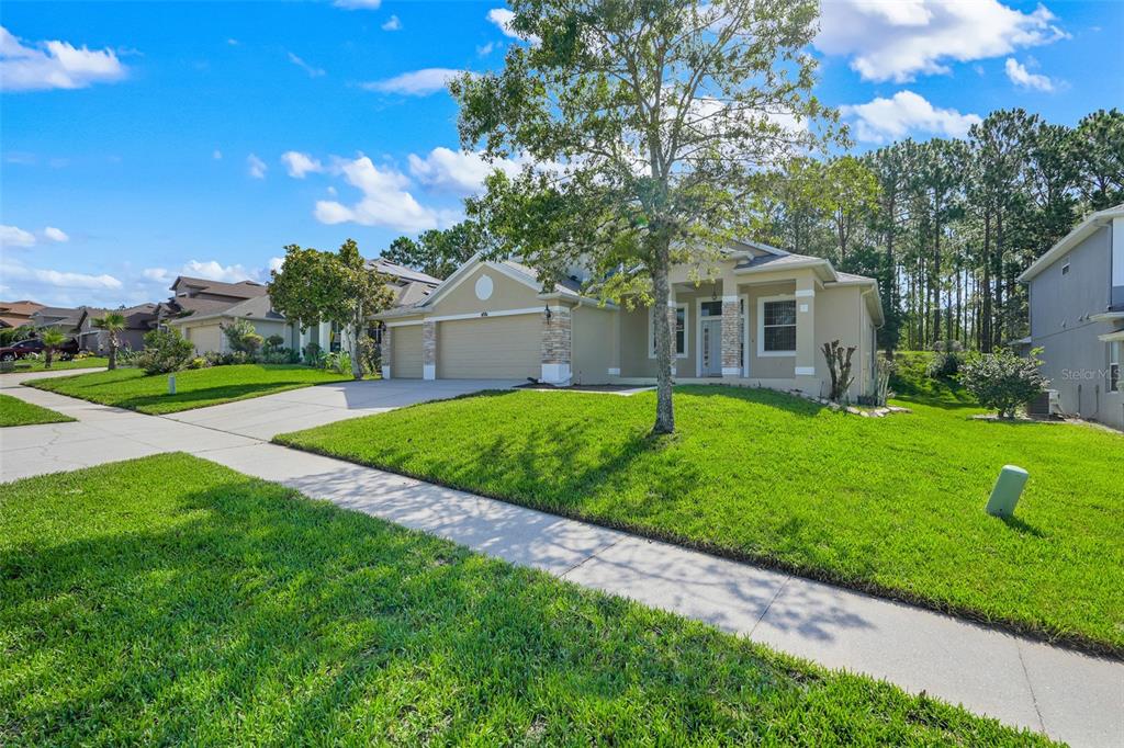 A single-story suburban house with a tan exterior, stone accents, and a two-car garage — 1832 NATURE COVE LANE, CLERMONT, FL