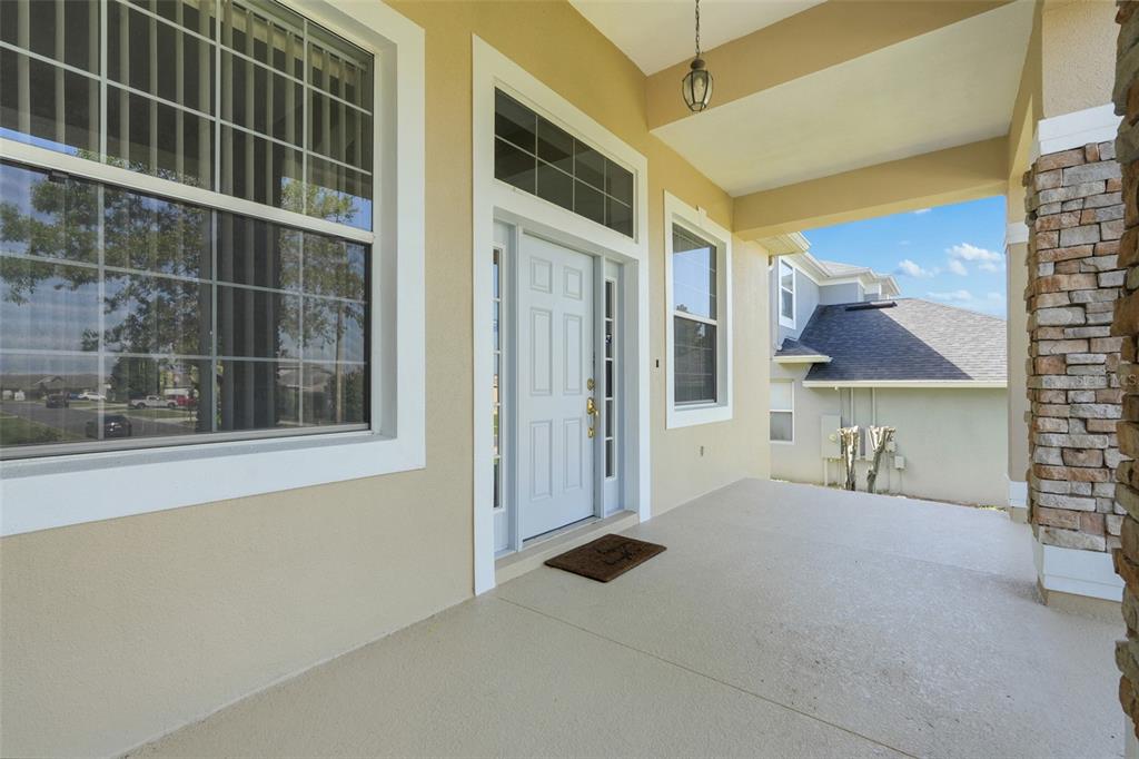 A covered front porch with a light-colored door, stone pillar, and large window — 1832 NATURE COVE LANE, CLERMONT, FL