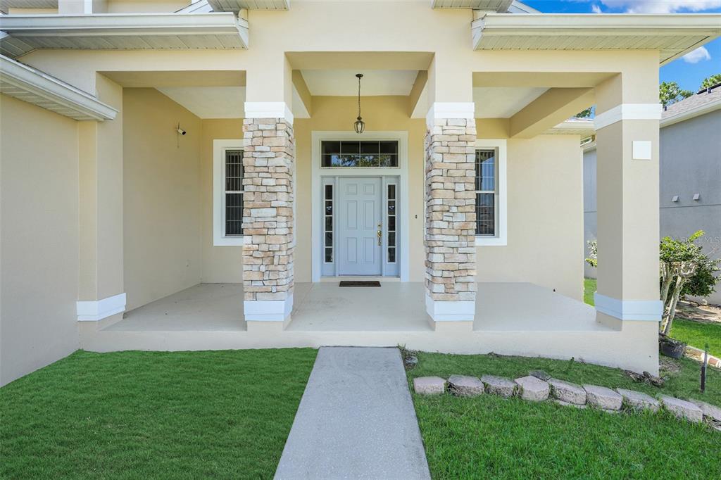 A front porch with stone-accented columns leads to a light blue front door — 1832 NATURE COVE LANE, CLERMONT, FL