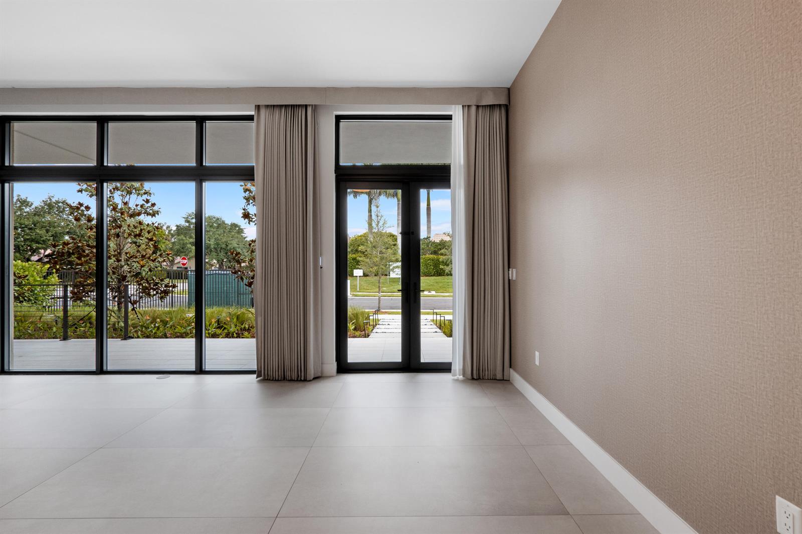 An empty room with large windows, glass doors, light tile flooring, and textured beige walls — 16788 Natures Way, Weston FL 33326, WESTON, FL