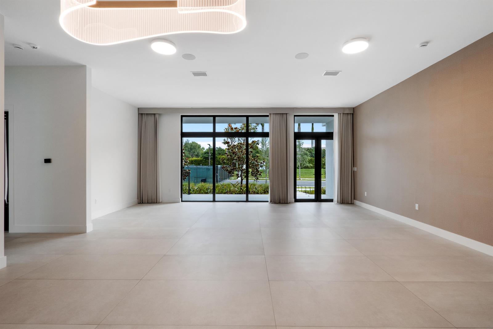 An empty room features large windows, light tile flooring, and a modern light fixture — 16788 Natures Way, Weston FL 33326, WESTON, FL