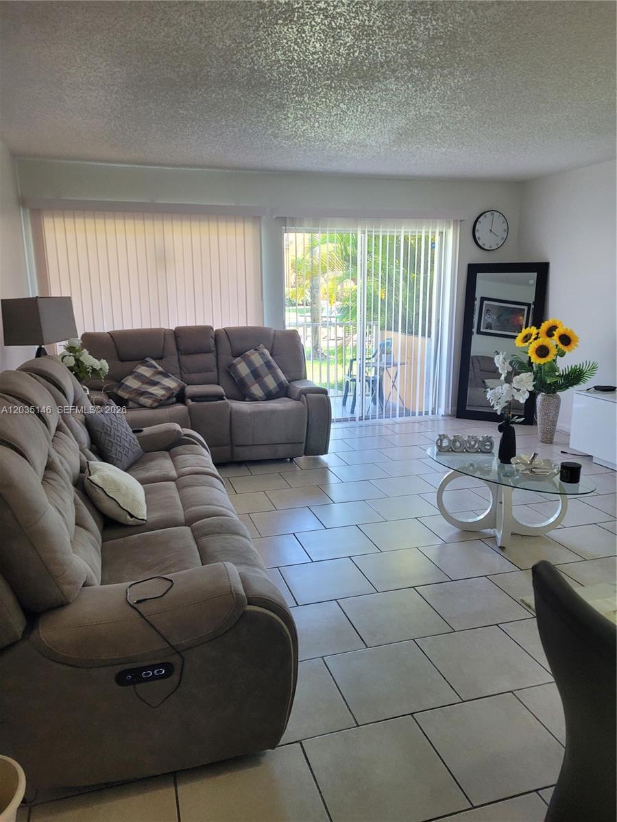 A living room features light tile flooring, two brown reclining sofas, and a glass coffee table — 18101 NW 68th Ave # E105, Hialeah FL 33015, HIALEAH, FL