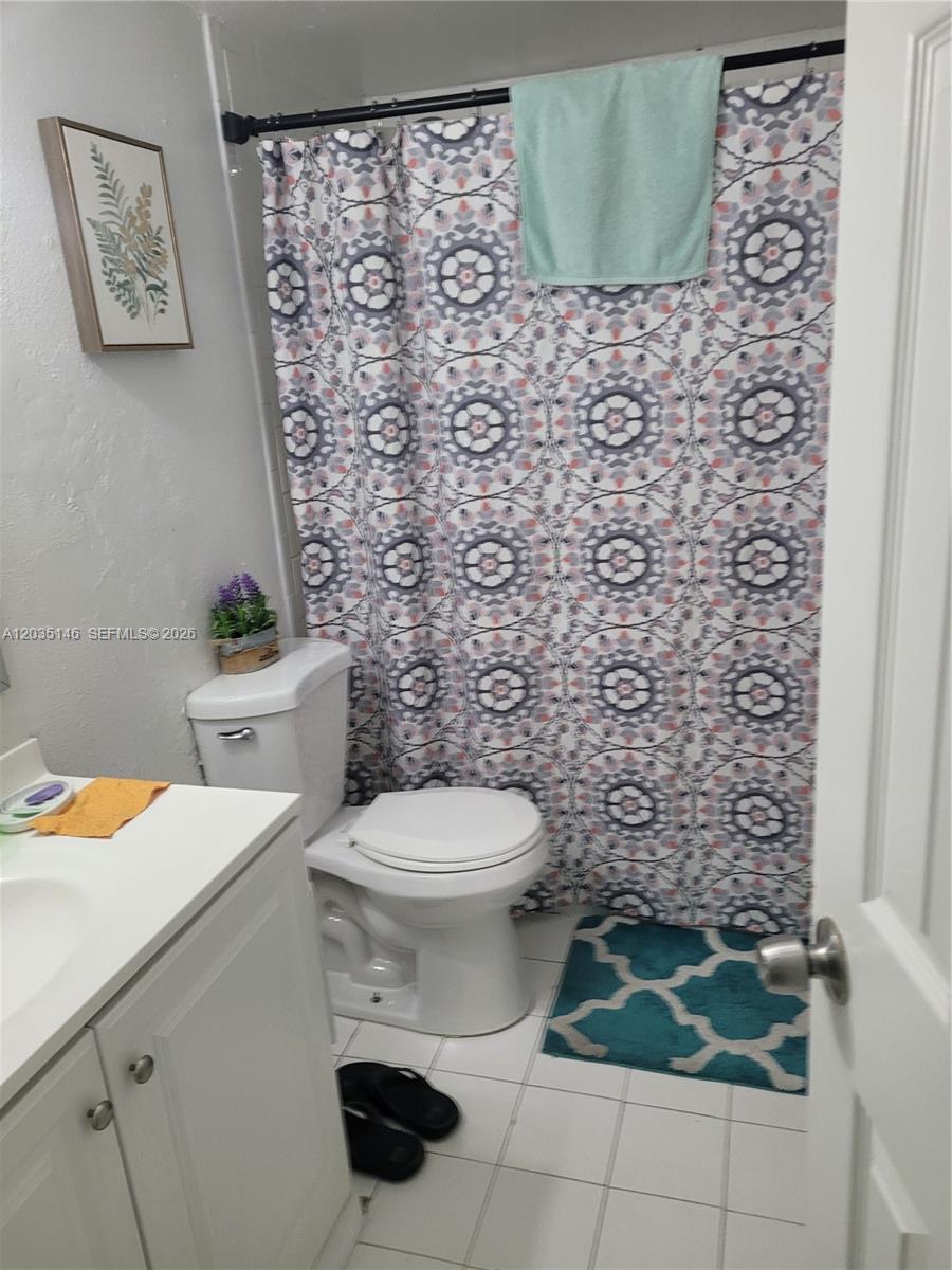 A bathroom features a white vanity, a toilet, and a patterned shower curtain — 18101 NW 68th Ave # E105, Hialeah FL 33015, HIALEAH, FL