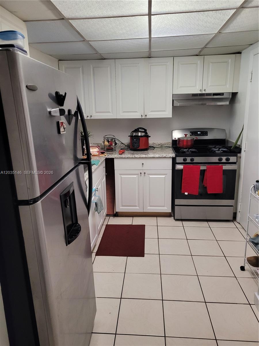 A kitchen features white cabinets, stainless steel appliances, granite countertops, and light-colored tile flooring — 18101 NW 68th Ave # E105, Hialeah FL 33015, HIALEAH, FL