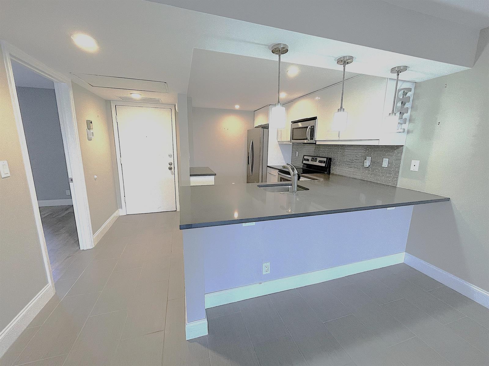A kitchen with a grey quartz breakfast bar, white cabinets, and stainless steel appliances — 3 Royal Palm Way # 205, Boca Raton FL 33432, BOCA RATON, FL