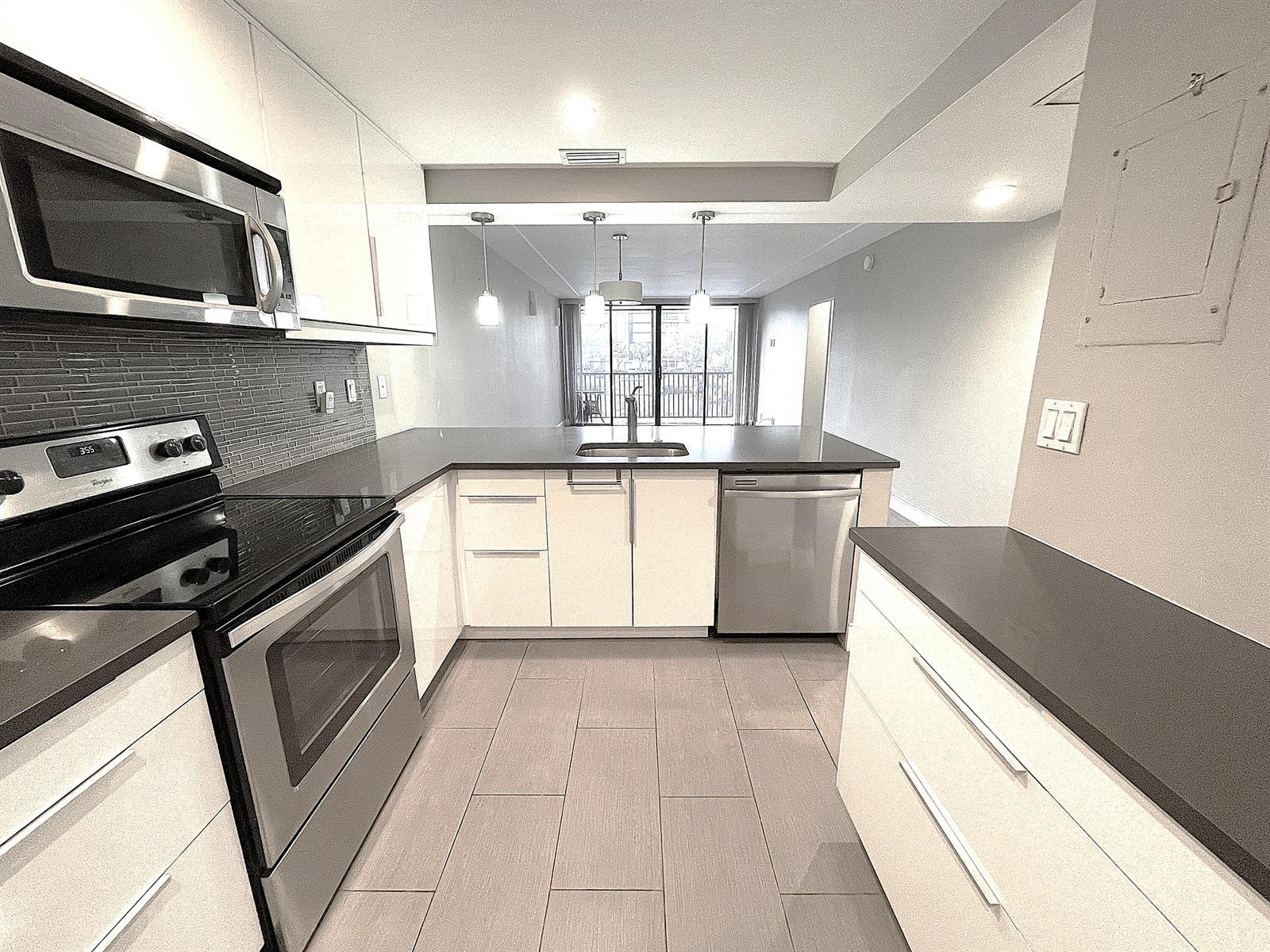 A modern kitchen features white cabinets, stainless steel appliances, dark countertops, and tile flooring — 3 Royal Palm Way # 205, Boca Raton FL 33432, BOCA RATON, FL