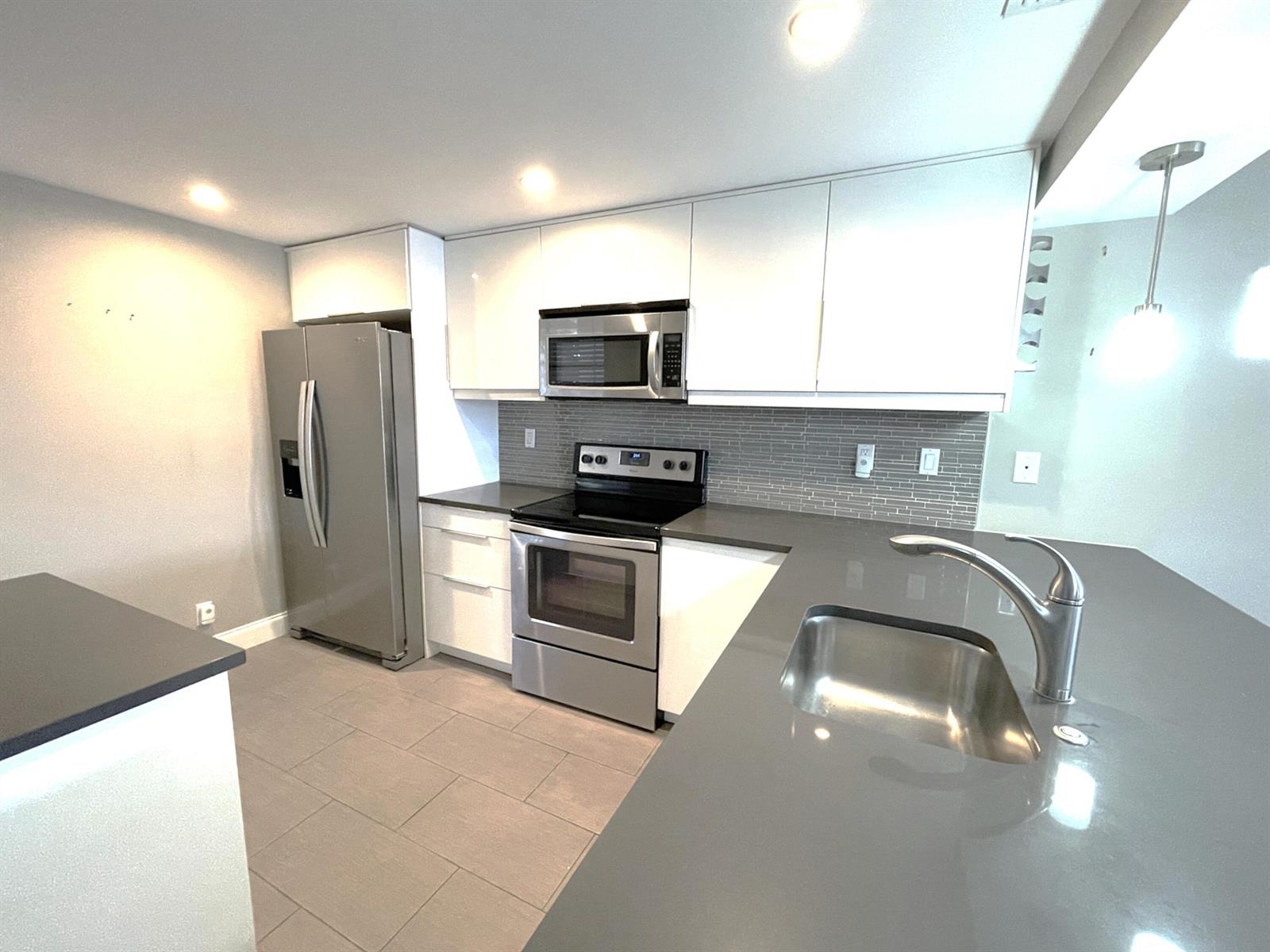 A modern kitchen features white cabinets, stainless steel appliances, and gray quartz countertops — 3 Royal Palm Way # 205, Boca Raton FL 33432, BOCA RATON, FL