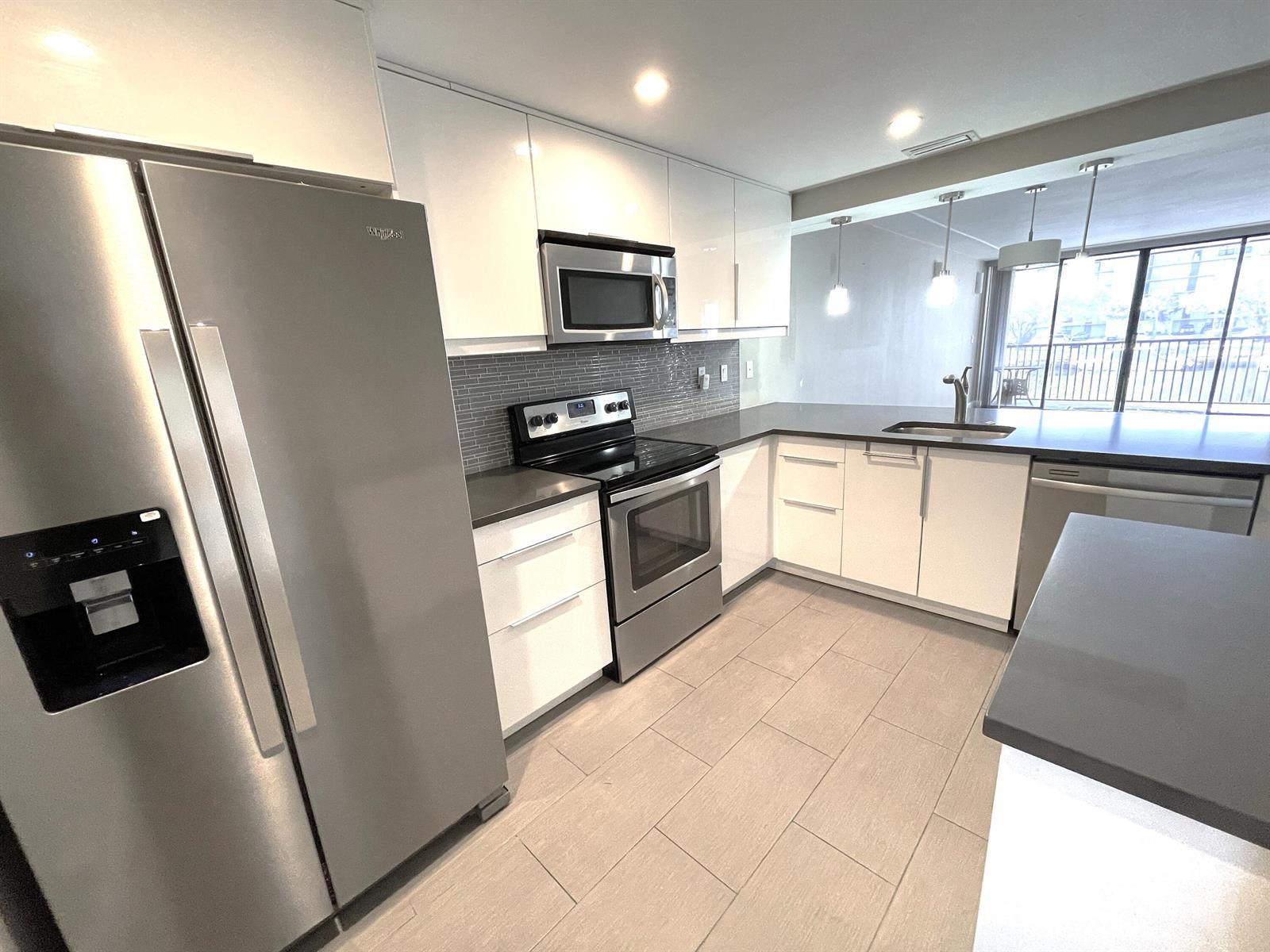 A modern kitchen features white cabinets, stainless steel appliances, gray countertops, and tile flooring — 3 Royal Palm Way # 205, Boca Raton FL 33432, BOCA RATON, FL