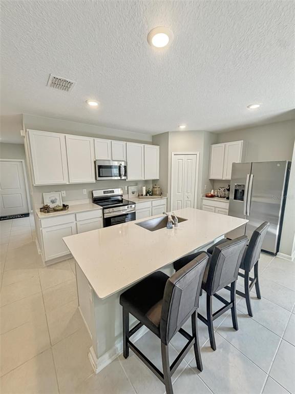 A kitchen features white cabinetry, stainless steel appliances, a central island, and light-colored tile flooring — 1363 BLUE ASH LANE, DELAND, FL