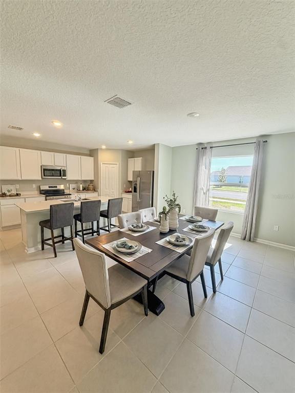 A kitchen with white cabinets and an island opens into a dining area with tile floors — 1363 BLUE ASH LANE, DELAND, FL