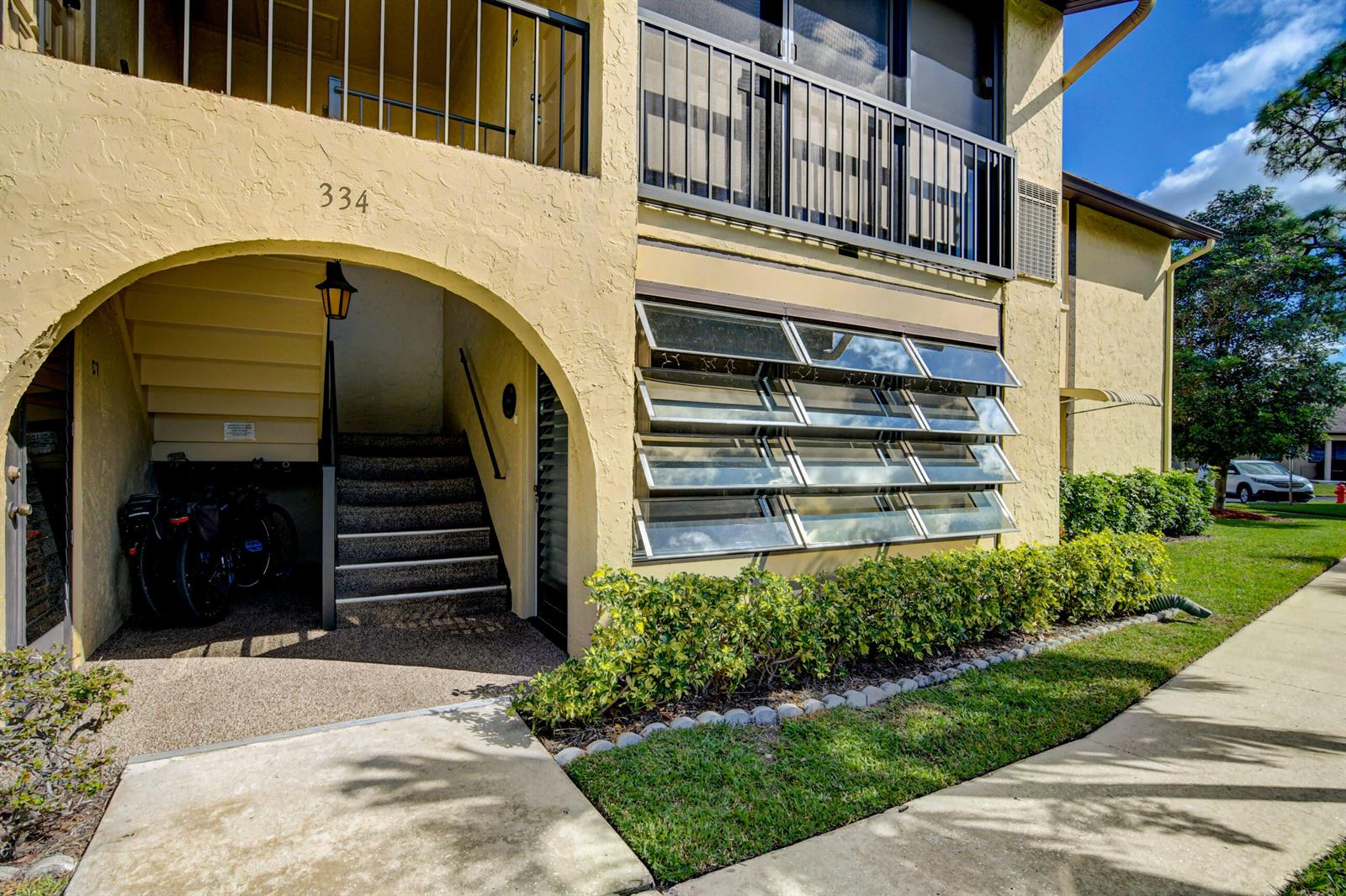A yellow stucco building exterior features an arched entryway, stairs, and louvered glass windows — 334 Pine Ridge Circle # 1, FL 33463, FL