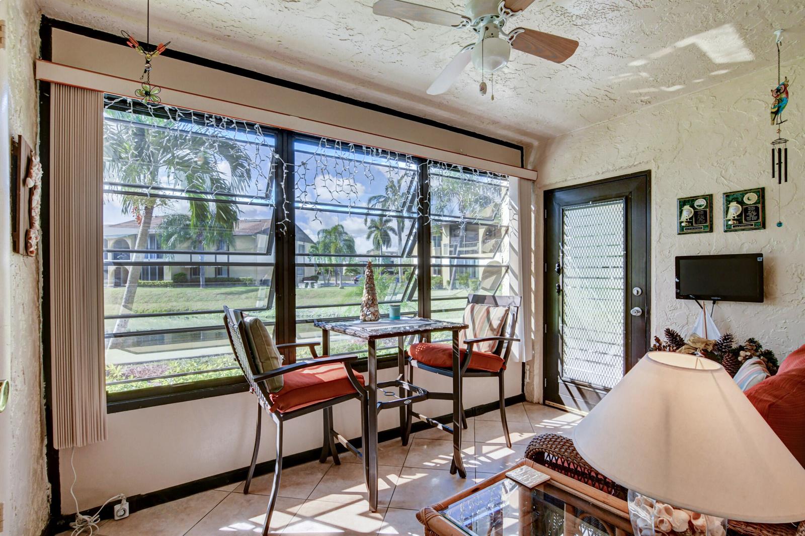 A sunroom features a dining set by large windows overlooking a canal and palm trees — 334 Pine Ridge Circle # 1, FL 33463, FL