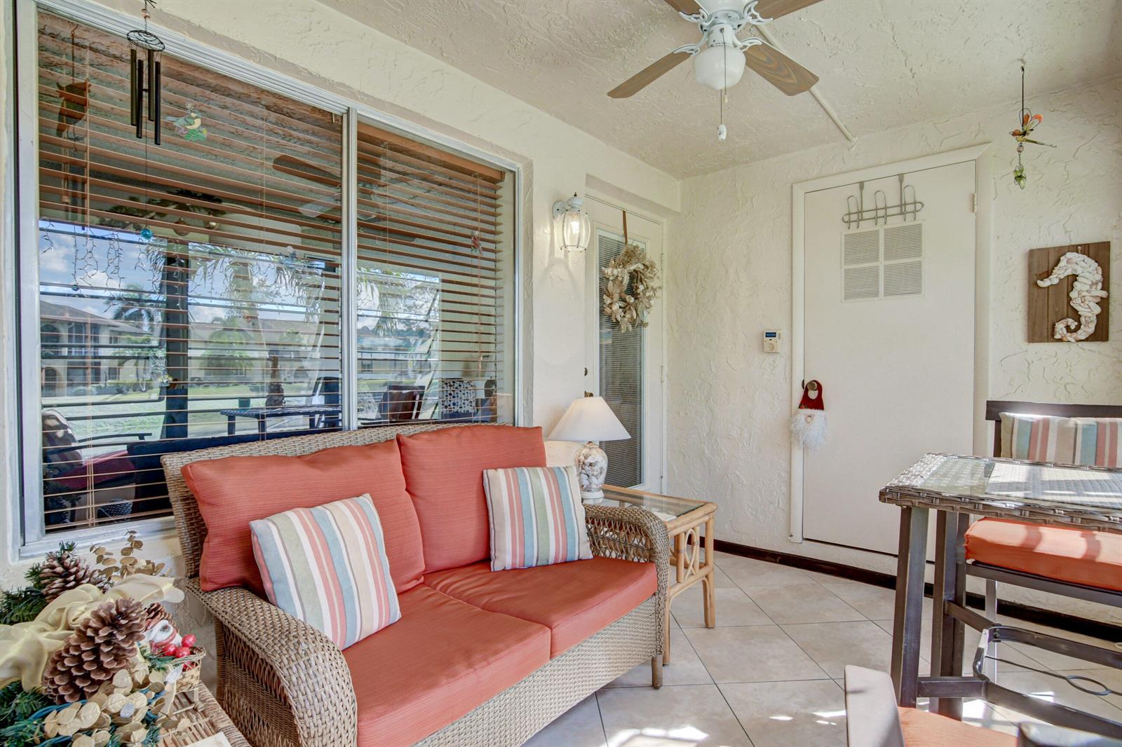 A sunroom features a wicker sofa with orange cushions, a ceiling fan, and tiled flooring — 334 Pine Ridge Circle # 1, FL 33463, FL