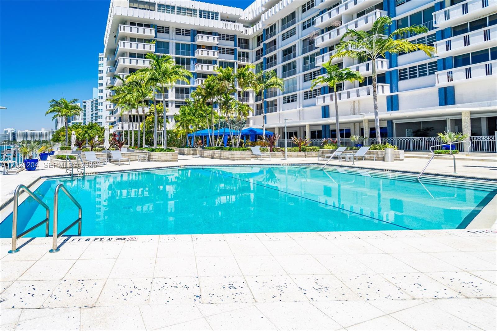 A swimming pool sits in front of a multi-story white building with blue accents — 800 West Ave # 509, Miami Beach FL 33139, MIAMI BEACH, FL