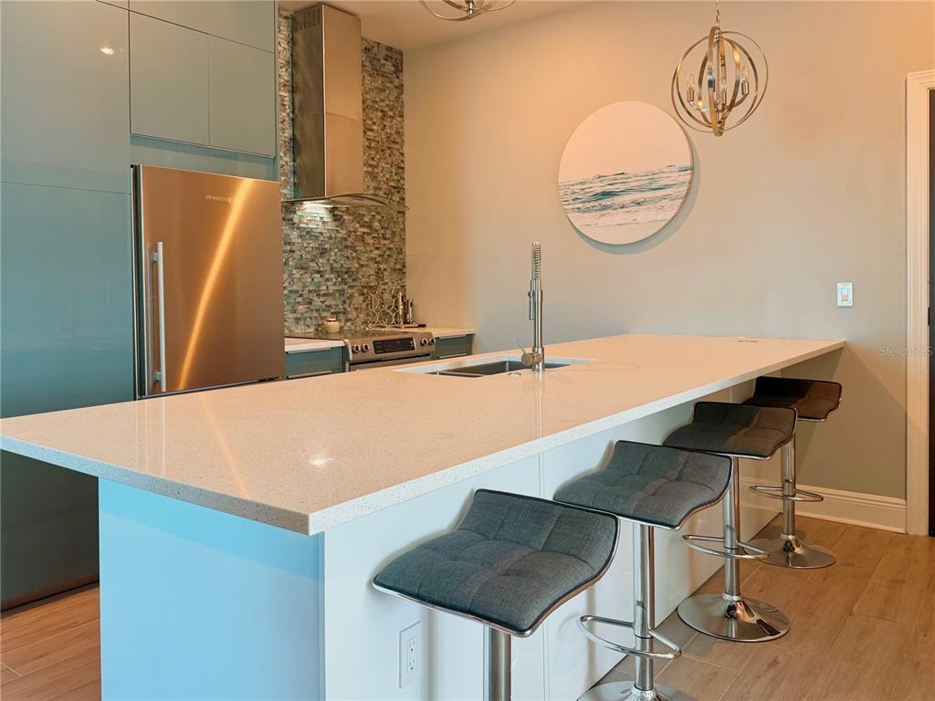 A modern kitchen features a long white quartz island, bar stools, and blue cabinetry — 1238 E KENNEDY BOULEVARD UNIT 1001, TAMPA, FL