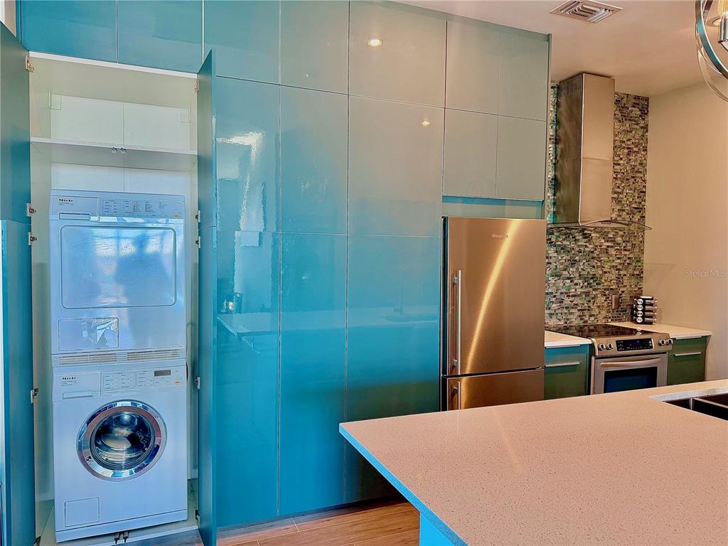 A kitchen features teal cabinetry, a stacked washer and dryer, and stainless steel appliances — 1238 E KENNEDY BOULEVARD UNIT 1001, TAMPA, FL