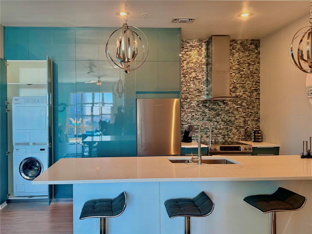 A modern kitchen features teal cabinetry, a stainless steel refrigerator, and a stacked laundry unit — 1238 E KENNEDY BOULEVARD UNIT 1001, TAMPA, FL