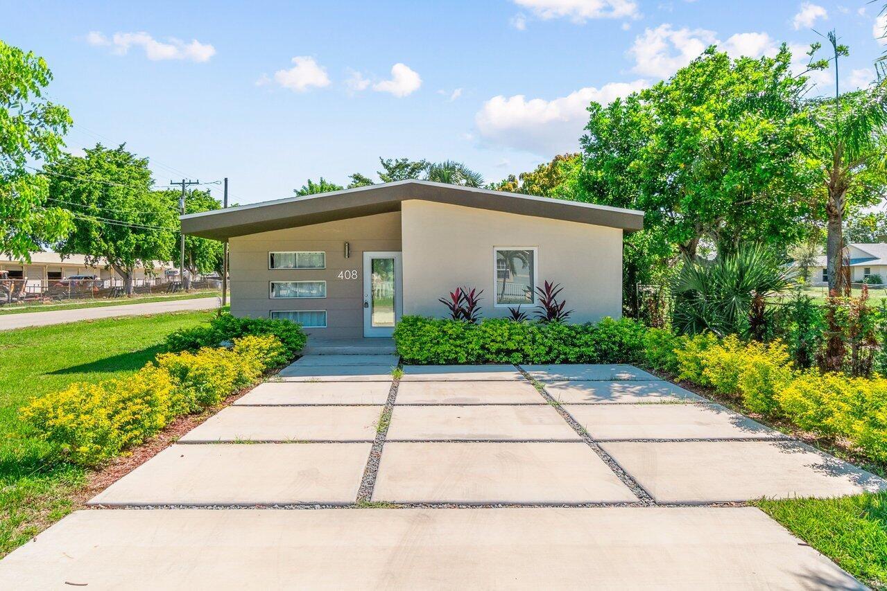 A single-story house with a flat roof, concrete driveway, and landscaping under a blue sky — 408 SW 4th Street, Delray Beach FL 33444, DELRAY BEACH, FL