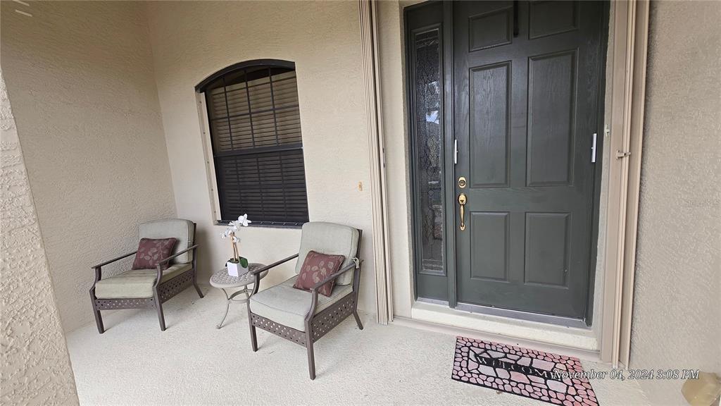 A covered front porch features two chairs, a small side table, and a dark front door — 24412 LAKEVIEW PLACE, PUNTA GORDA, FL