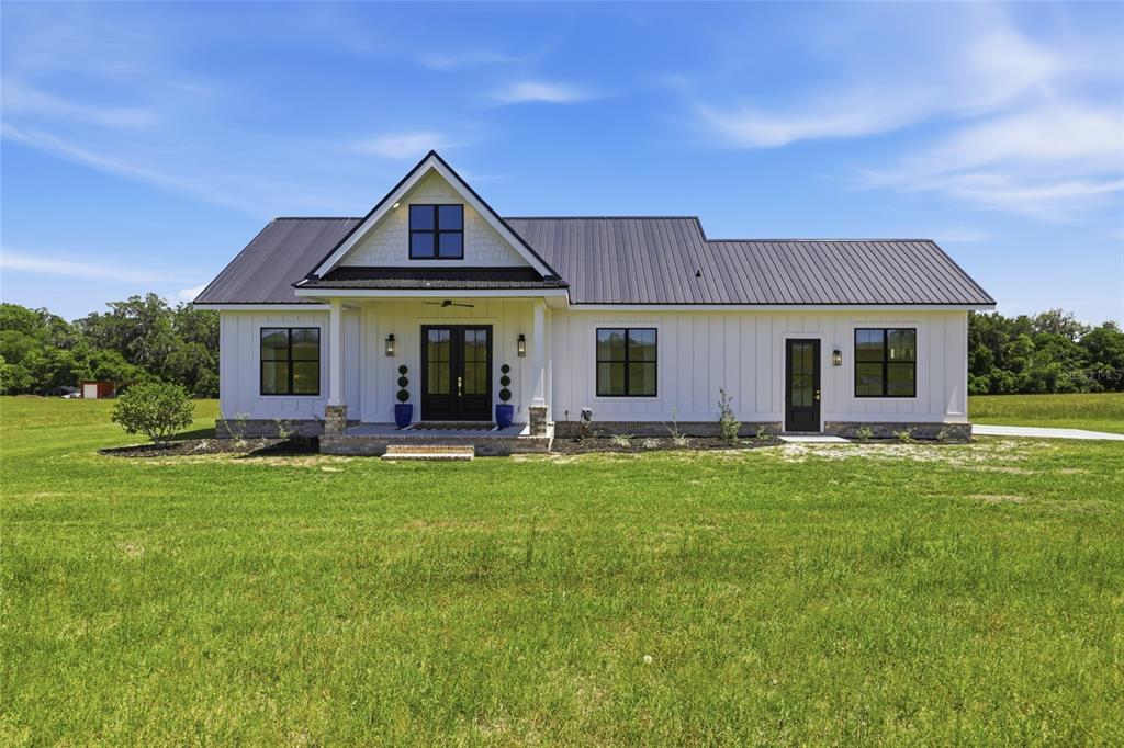 A white farmhouse with a metal roof and a front porch sits on a grassy lot — 18605 NW COUNTY ROAD 235A, ALACHUA, FL